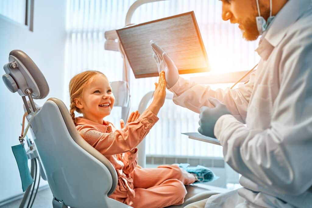 A young girl sitting in a dentist’s chair, smiling brightly during National Smile Day at Orthodontics Thibodaux.